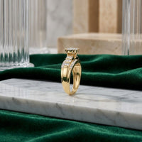 The 10k Gold Round Diamond Heart Engagement Ring is showcased on a marble surface, featuring a striking central diamond flanked by sparkling side stones. Surrounded by green velvet fabric and glass columns in the background, this elegant ring radiates timeless sophistication and romantic charm.