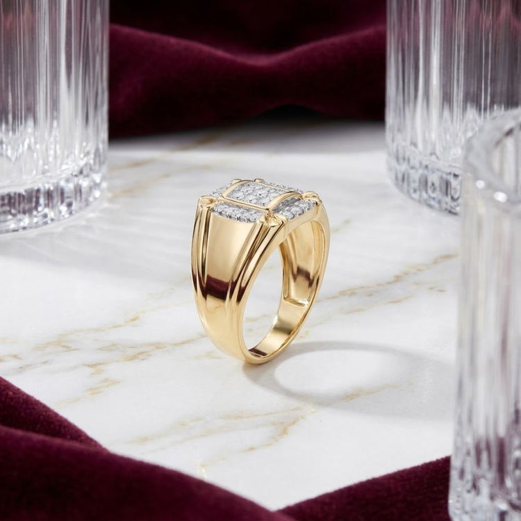 A breathtaking 10K Yellow Gold Diamond Cluster Ring 1/4CT, adorned with shimmering square-cut diamonds, rests on a white marble surface amid clear glass tumblers and rich burgundy velvet fabric.