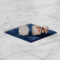 A pair of 10k Gold Diamond Cluster Earrings – 1/8 Cttw rests on a dark blue square velvet pad placed on a white marble surface.