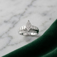 A 10k gold oval diamond cluster bridal ring (1/2 cttw) is displayed on a white marble surface next to a piece of dark green velvet fabric.
