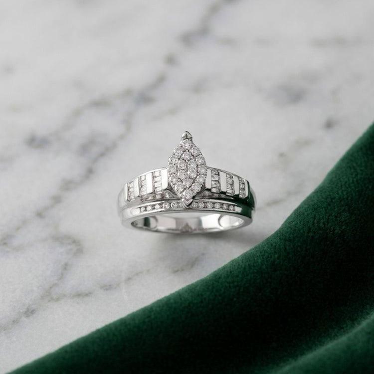 A 10k gold oval diamond cluster bridal ring (1/2 cttw) is displayed on a white marble surface next to a piece of dark green velvet fabric.