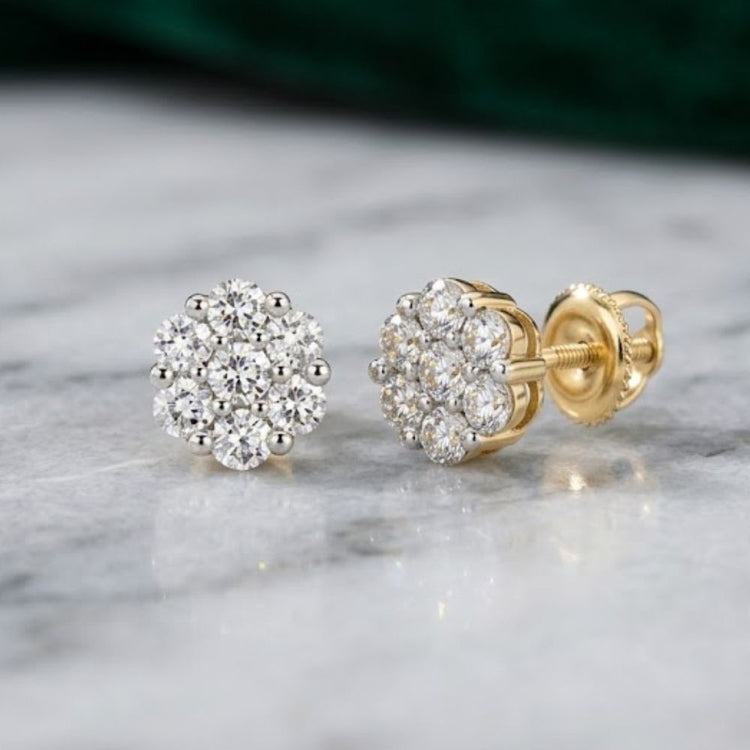 A pair of 10k Gold Diamond Flower Cluster Earrings 1 Cttw, each showcasing a cluster of natural round diamonds in an elegant floral design, displayed on a marble surface.