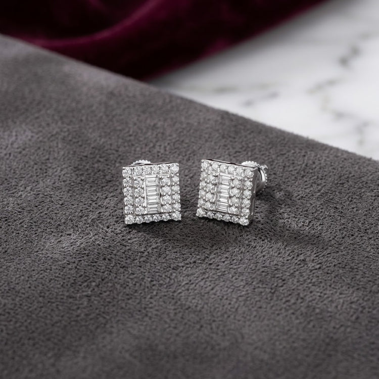 A pair of 10K Gold Diamond Square Earrings 1/2 CTTW with a double halo design, showcased on a gray suede surface accented by marble and burgundy fabric in the background.