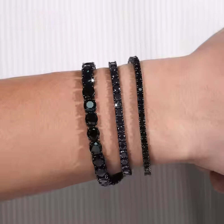 A wrist displays three Black Moissanite Tennis Bracelets of different thicknesses, all set in 925 sterling silver, against a light striped background.