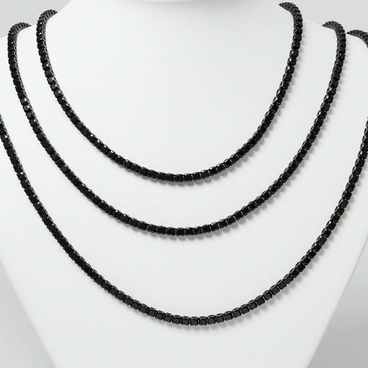 The Black Moissanite Tennis Chain - 3mm is showcased on a white necklace stand, highlighting its sleek design, shiny black stones, and uniform round shape.
