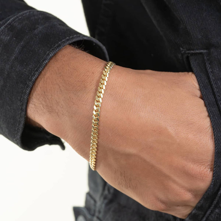 A close-up shows a hand wearing the Cuban Link Bracelet - 6mm, paired with a black denim jacket and one hand partly tucked in the pocket, set against a simple light background.