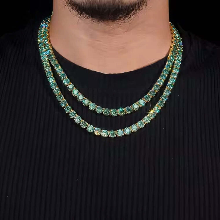 A person wearing a black ribbed shirt and two gold chains, one being the Green Moissanite Tennis Chain - 3mm with sparkling turquoise gemstones, both layered closely around their neck.