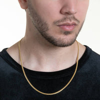 A man with a short beard models the Cuban Link Chain Solid Gold - 3mm over a black shirt. Only his lower face, neck, and upper chest are shown against a plain light background.