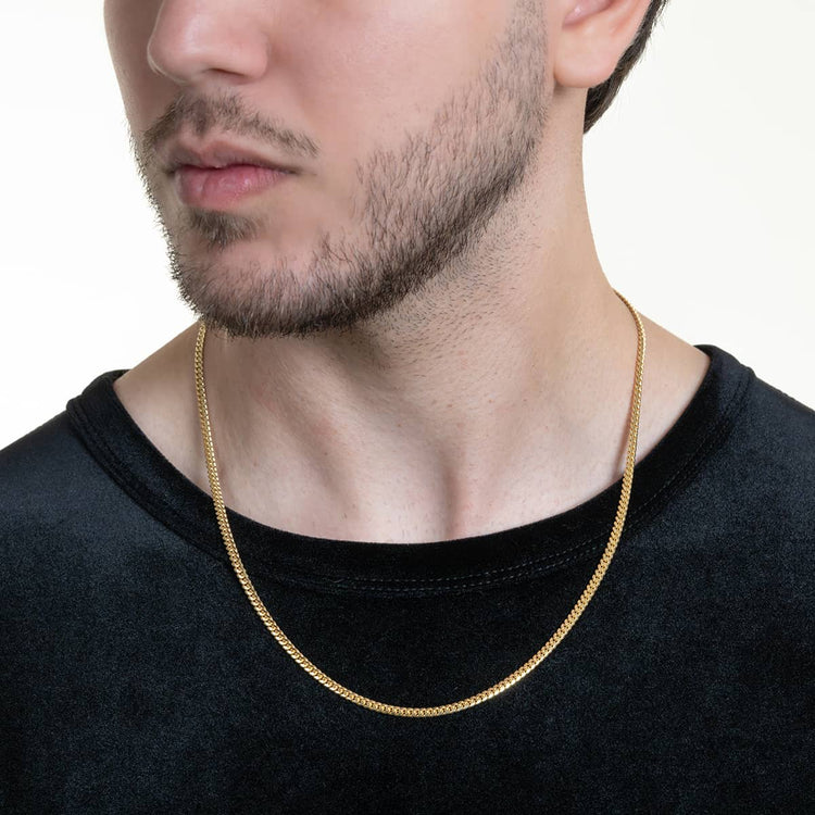 A man with light skin and short facial hair wears a black shirt and the Cuban Link Chain Solid Gold - 3mm around his neck, set against a plain, light-colored background.