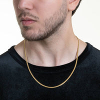 A man with light skin and short facial hair wears a black shirt and the Cuban Link Chain Solid Gold - 3mm around his neck, set against a plain, light-colored background.