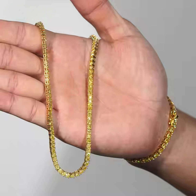 A hand holds the Yellow Moissanite Tennis Chain - 3mm, its textured gold design and sparkling stones shining brightly, resembling a matching bracelet against a plain background.