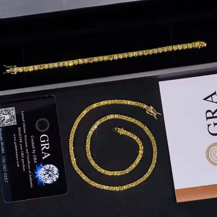 The Yellow Moissanite Tennis Chain - 3mm and a matching gold necklace with sparkling stones are presented in a black box, accompanied by a GRA certification card and a white envelope featuring the GRA logo.