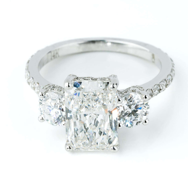 The 4.84 CTW 14k White Gold Three Stone Radiant Engagement Ring showcases a radiant center stone, two round side diamonds, and accent diamonds on the band.