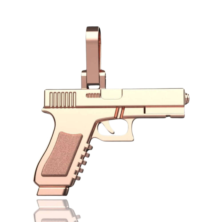 The 14k Gold Pistol Pendant, crafted in rose gold and shaped like a handgun with a chain loop, is shown against a white background with a subtle reflection beneath.