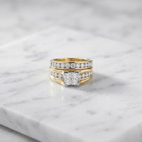 Introducing the 14K Gold Princess Diamond Bridal Ring Set 2 CTTW, featuring a stunning three-band design encrusted with sparkling diamonds and showcasing a central square-cut princess diamond, beautifully displayed on a white marble surface.