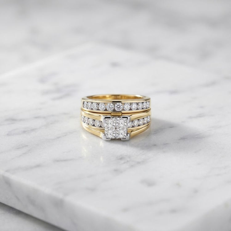 Introducing the 14K Gold Princess Diamond Bridal Ring Set 2 CTTW, featuring a stunning three-band design encrusted with sparkling diamonds and showcasing a central square-cut princess diamond, beautifully displayed on a white marble surface.
