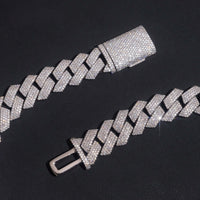 A close-up of the Moissanite Cuban Links Chain 18mm - 925 Sterling Silver, featuring a box clasp, is displayed on a black surface. Its metal links are encrusted with sparkling moissanite stones.