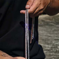 A person in a black shirt holds two sparkling tennis chains, including the Asscher Cut Moissanite Tennis Chain - 4mm, against a blurred outdoor background.