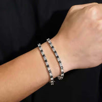 A close-up of a wrist wearing the Black Moissanite Tennis Bracelet - 4mm, featuring alternating black and white stones set in 925 sterling silver, against a black background.