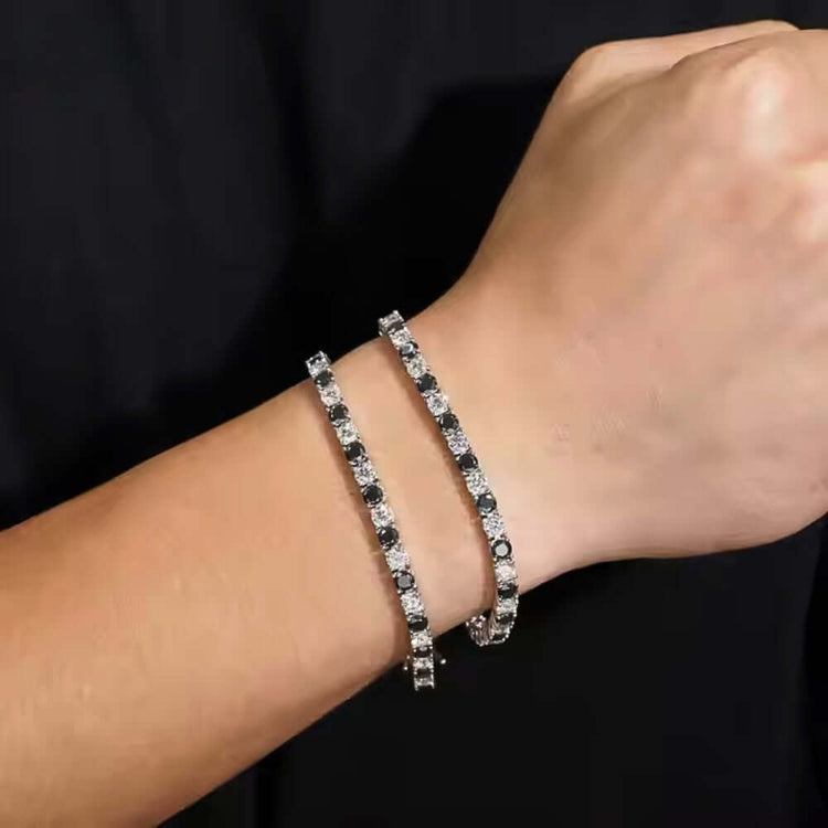 A close-up of a wrist wearing the Black Moissanite Tennis Bracelet - 4mm, featuring alternating black and white stones set in 925 sterling silver, against a black background.