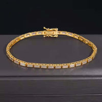 The Emerald Moissanite Tennis Bracelet - 4mm, featuring rectangular gold links and clear emerald-cut moissanite gemstones, is displayed on a dark, smooth surface against a black background.