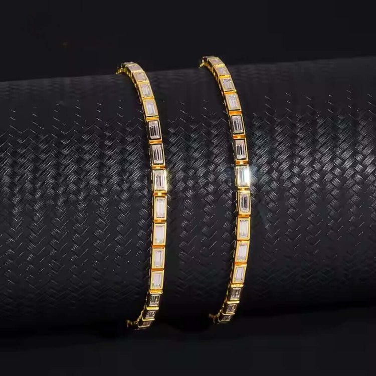 The Emerald Moissanite Tennis Bracelet - 4mm features square and rectangular stones in a repeating pattern, reminiscent of emerald-cut moissanite, elegantly showcased on a textured black cylindrical display.