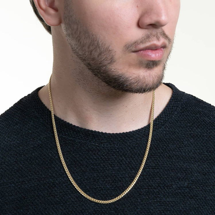 A man wearing a textured dark shirt and the Cuban Link Chain Solid Gold 4mm - Box Lock, shown from the shoulders up, his face partially visible and turned slightly to the side against a light background.