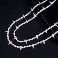 The Thorny Moissanite Tennis Chain - 4mm, featuring alternating round and triangular spike-shaped links, is displayed alongside another diamond-studded necklace on a glossy black surface.
