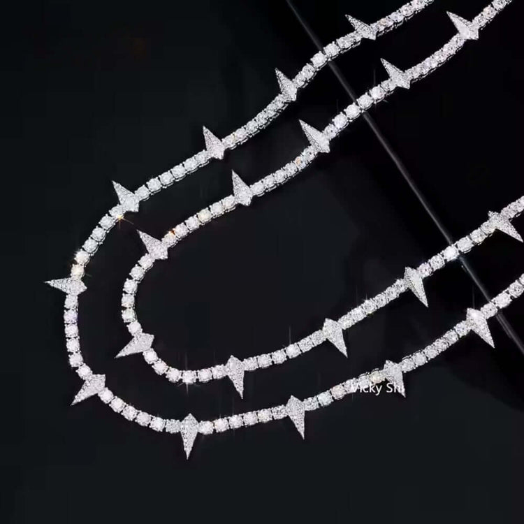 The Thorny Moissanite Tennis Chain - 4mm, featuring alternating round and triangular spike-shaped links, is displayed alongside another diamond-studded necklace on a glossy black surface.