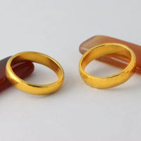 Two simple 4mm, 24k Band Rings rest on a white surface, each wedding ring elegantly placed atop a reddish-brown, translucent decorative stone.