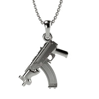 The 14k Gold Mini Draco Pendant, shaped like a submachine gun and paired with bold gold jewelry, is displayed against a plain white background.