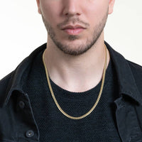 A man wears a black textured shirt, black jacket, and the Cuban Link Chain Solid Gold 5mm - Box Lock. Only the lower half of his face and upper torso are visible, set against a light background.