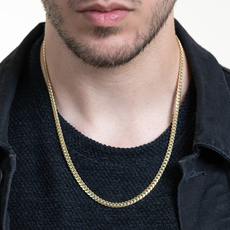 Close-up of a man wearing the Cuban Link Chain Solid Gold 5mm - Box Lock over a black textured shirt and black jacket, with his partially visible face showing a trimmed beard and mustache.