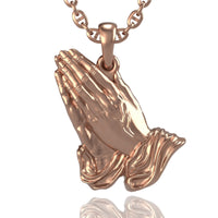 The 14k Gold Praying Hands Pendant showcases two hands in prayer with draped sleeves, beautifully detailed and displayed against a white background.