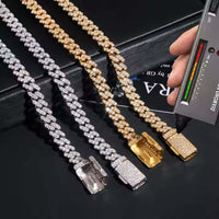 Three Moissanite Cuban Link Chains - 6mm, two in 925 sterling silver and one in gold, shine on a black surface as a hand tests the clasp of the VVS moissanite gold chain with a diamond tester.