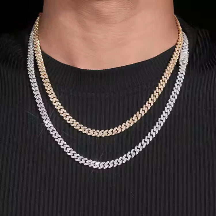 Wearing a ribbed black shirt, the person showcases two Cuban link chains: a gold one and a 6mm Moissanite Cuban Link Chain crafted from 925 sterling silver, both layered around the neck with a shiny, reflective finish.