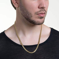 A man wears a black, semi-sheer shirt and the Cuban Link Chain Solid Gold 6mm - Box Lock, shown from the shoulders up against a plain white background.