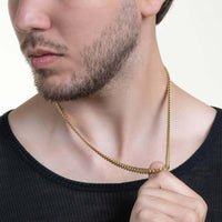 A man with a trimmed beard in a black shirt holds the Cuban Link Chain Solid Gold 6mm - Box Lock around his neck, his face partially visible as he gazes to the side.