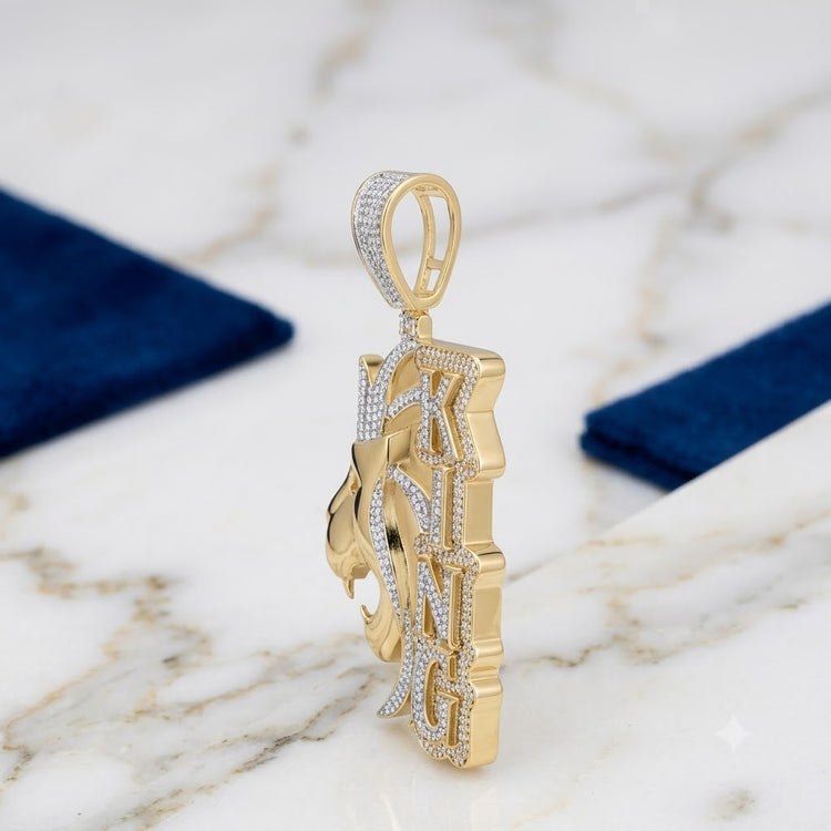 The 10K Gold Diamond Lion King Charm 2.2 CTW is a men’s pendant shaped like a lion’s head with vertical KING block letters, encrusted with small natural diamonds, shown on white marble with blue rectangular fabrics in the background.