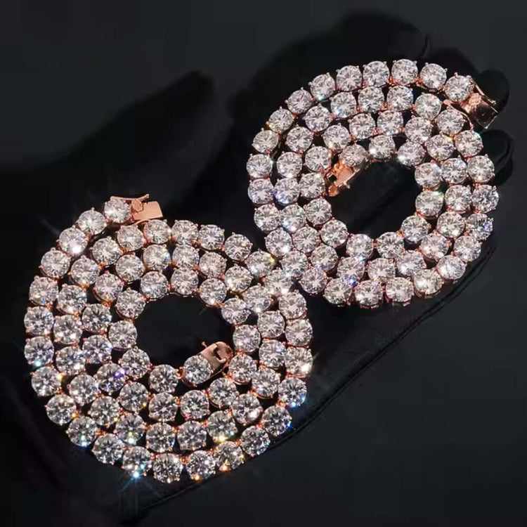 A hand in a black glove displays two gemstone-encrusted hoop earrings with a rose gold moissanite tennis chain (8mm), creating a dazzling, coordinated look.