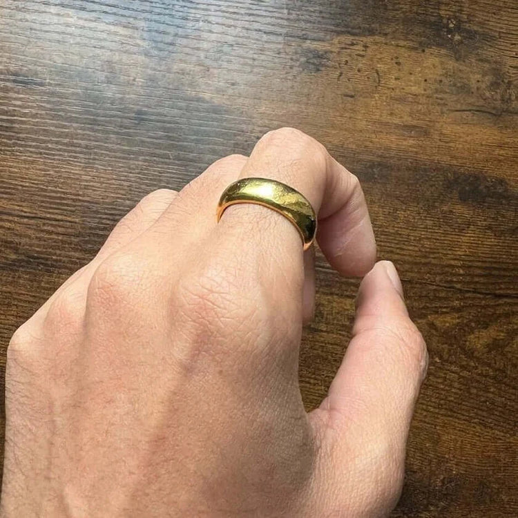 A hand displays the 8mm Band Ring -24k on the middle finger against a wooden surface.