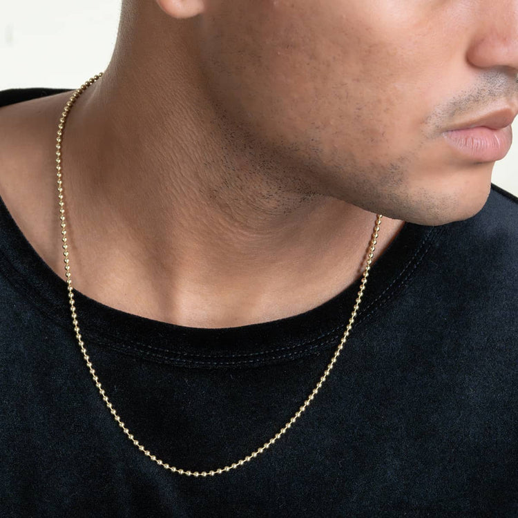 A close-up of a person wearing the Beads Chains 14K gold necklace over a black shirt, showing only their lower face, neck, and upper chest.