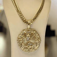 The Big Saint Lazarus Circular Pendant – 10K Solid Gold features a large, ornate religious design with intricate edging on a solid gold chain, elegantly displayed on a beige jewelry stand.