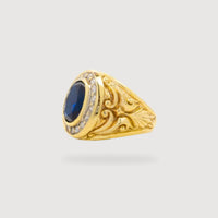 The Blue Stone Signet Ring in Solid Gold showcases a large oval blue stone at its center, encircled by small clear stones and ornate engravings, set against a plain light background.
