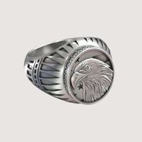 The Bold Eagle Liberty Statue Ring features an engraved eagle head with two stars on a circular face, accented by small gemstones and geometric patterns along the band.