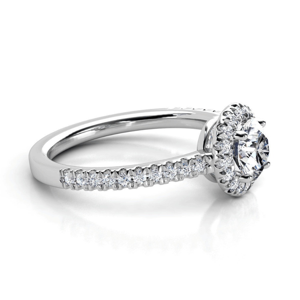 The Brilliance Halo Diamond Ring showcases a radiant round center diamond encircled by a shimmering halo, with pavé-set diamonds adorning its elegant white gold band.