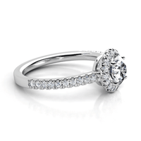 The Brilliance Halo Diamond Ring showcases a radiant round center diamond encircled by a shimmering halo, with pavé-set diamonds adorning its elegant white gold band.