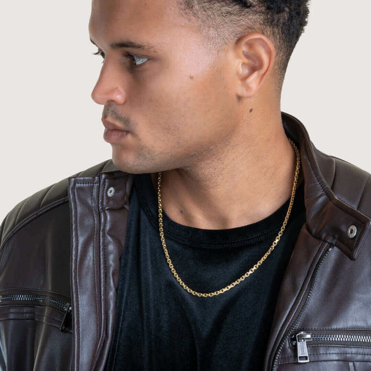 A man wearing a brown leather jacket, a black shirt, and the Cable Link Chain - 5mm gold necklace looks to his left against a light background.