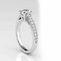 The Classic Round-Cut Lab Diamond Engagement Ring with Side Pave Details features a brilliant round lab diamond in four prongs, accented by sparkling side pave stones, elegantly shown on a white background.