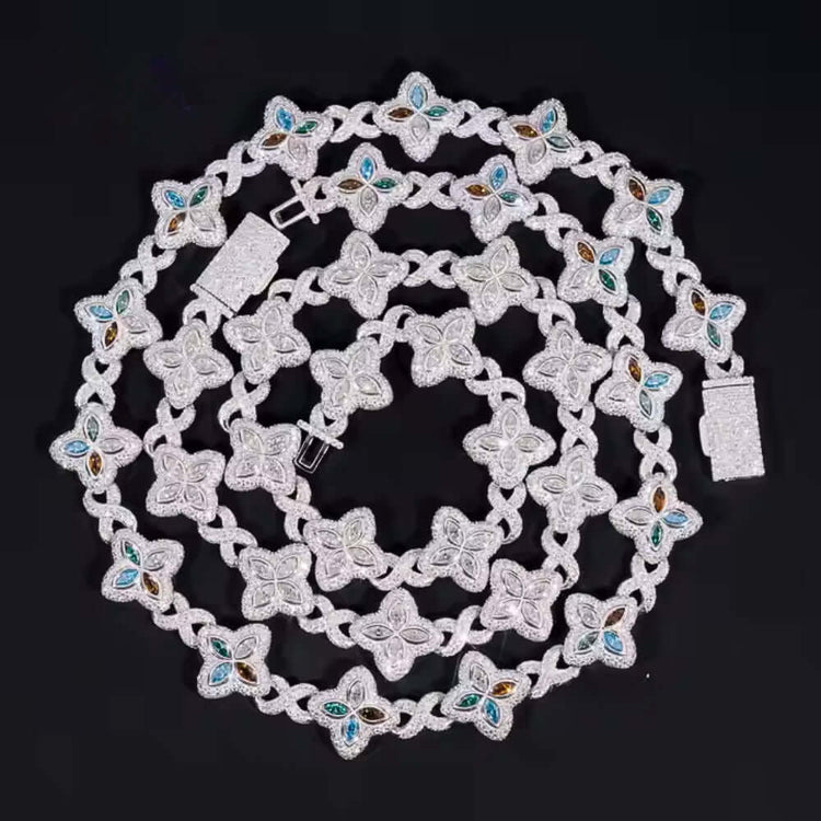 The Silver Clover Moissanite Chain, made from 925 sterling silver with flower-shaped links and blue and gold embellishments, is artfully coiled in a spiral on a black background.